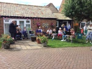 a group of people playing instruments in a garden on a sunny day