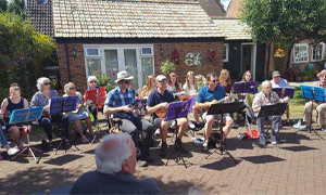 a group of people playing instruments in a garden on a sunny day