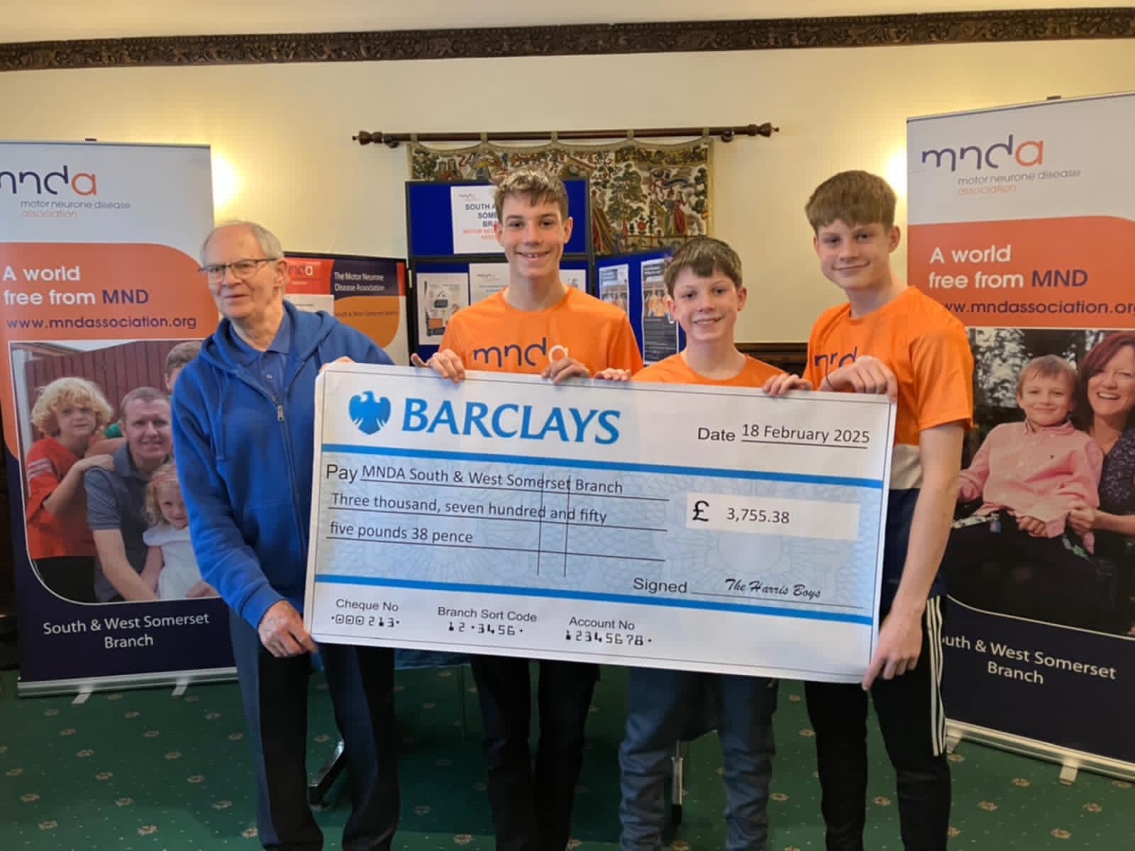 Branch treasurer Patrick dressed in blue accepting a cheque from the Harris boys 